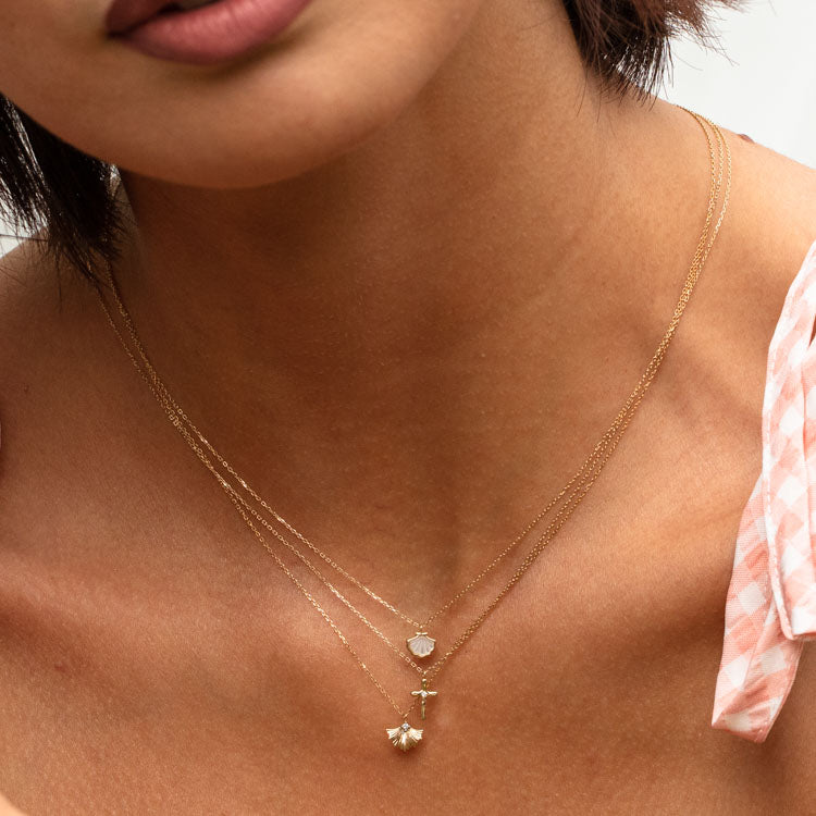 A woman wears the Solid Gold Ginkgo Leaf Diamond Necklace—a delicate 9k yellow gold chain with a diamond pendant—paired with a light pink checkered top.