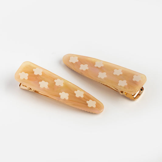 The Flower Barrette Set features two peach resin hair clips with gold clasps and white flower designs, creating a charming floral accessory displayed on a white background.