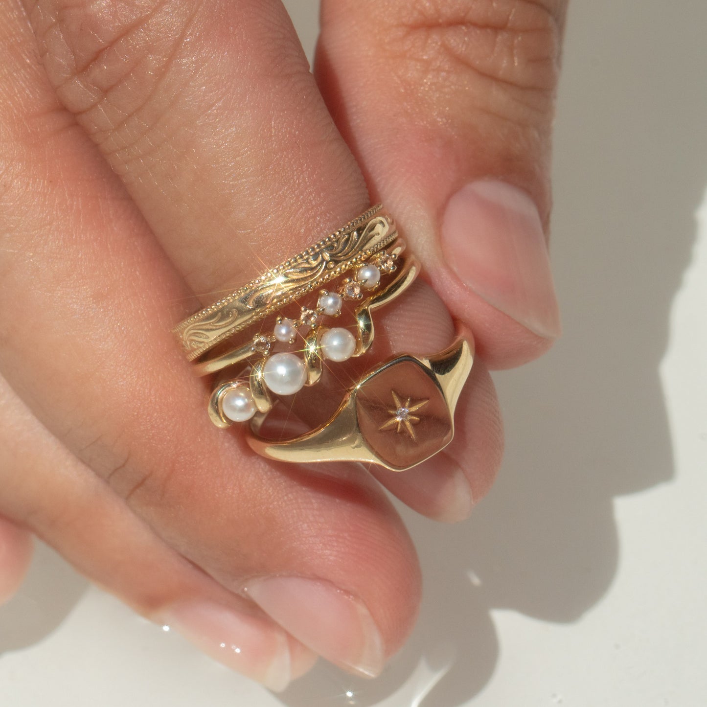 A close-up of a hand with natural nails, wearing three gold rings, including the Solid Gold Filigree Ring. Sunlight highlights the jewelry—featuring vintage filigree details—and the skin, creating a warm and elegant glow.