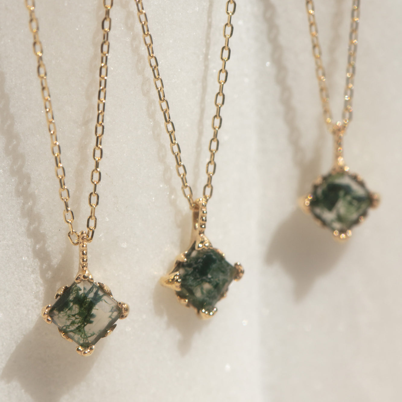 The Solid Gold Aquatic Agate Necklace for Grounding is displayed on a light, textured surface, showcasing green moss-like patterns beautifully set in gold.
