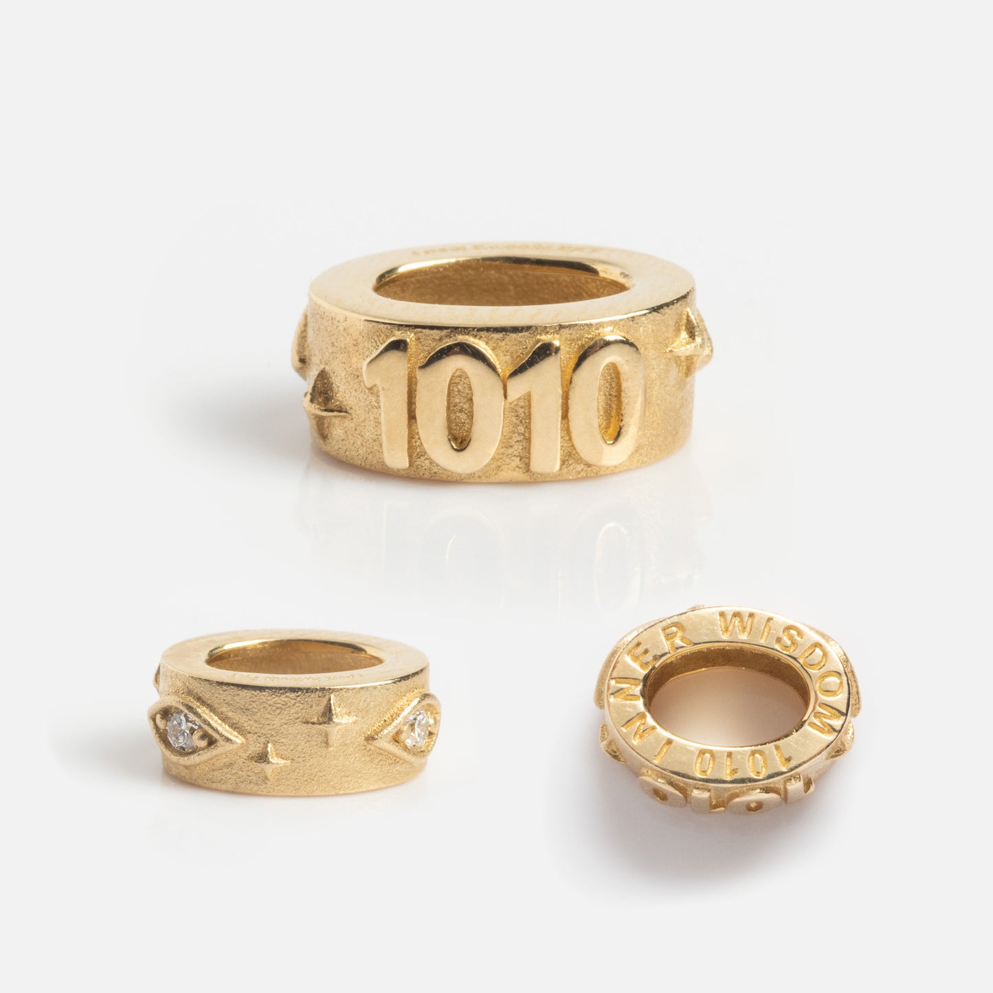 Three gold ring-shaped beads are displayed on a white background. This Local Eclectic Exclusive showcases the Solid Gold Angel Number Spacer Charm, including 1010 and diamond-accented designs.