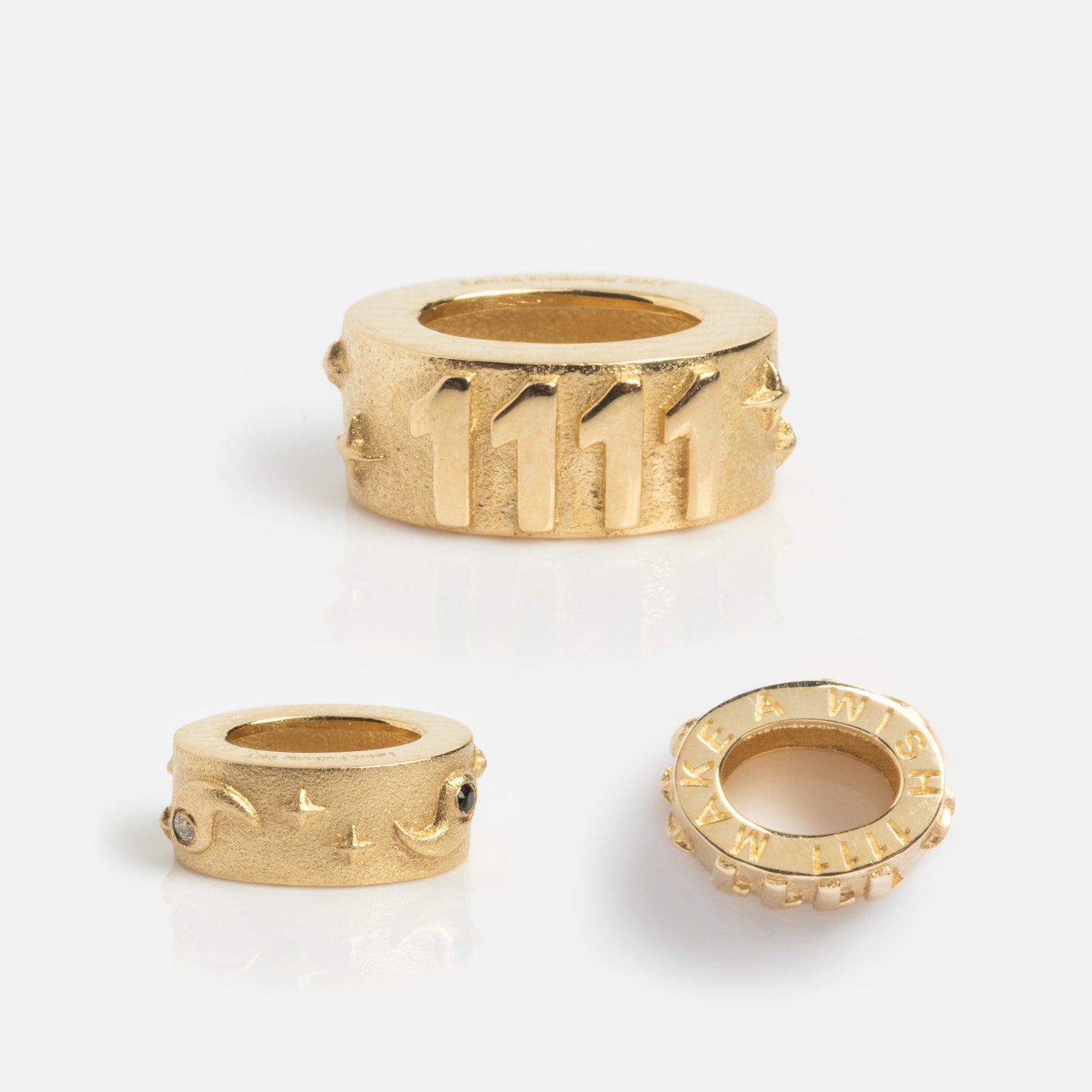 The Solid Gold Angel Number Spacer Charm, a Local Eclectic Exclusive, features “1111” engraving—perfect for angel number jewelry. Other charms include crescent moons with gems and one inscribed “MAKE A WISH” on its round edge.