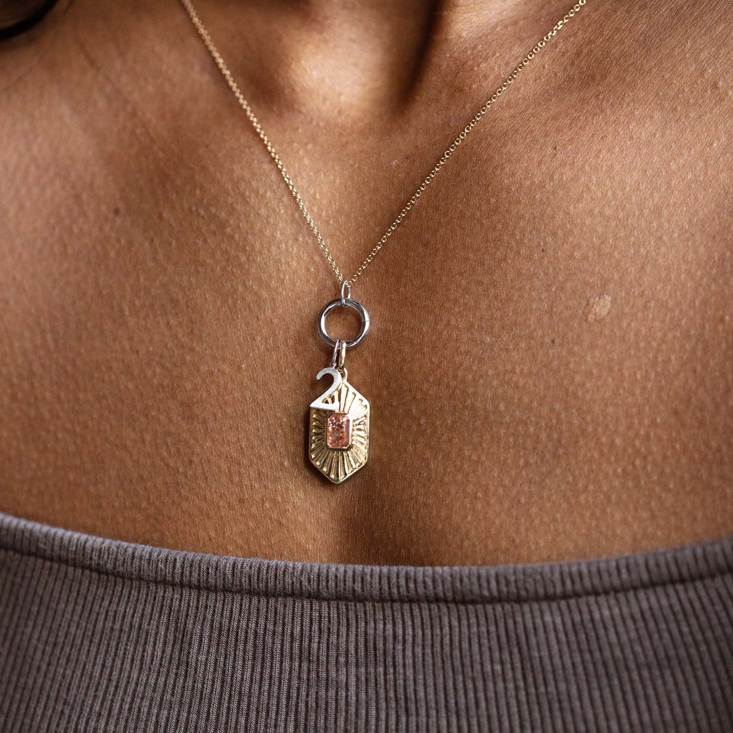 A close-up of a person wearing the Solid Gold Number Charm in White Gold on a thin chain, against bare skin and a ribbed gray off-shoulder top—ideal for those who love personalized jewelry.
