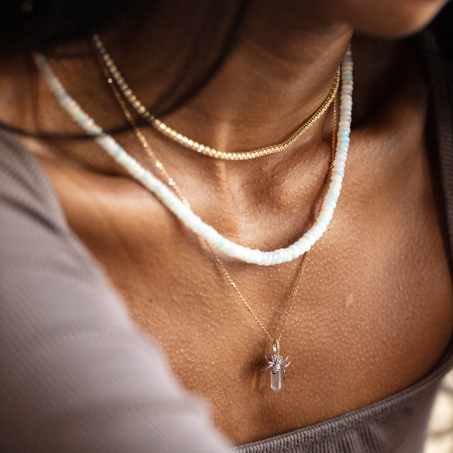 Close-up of a person wearing three necklaces: a thin gold chain, a beaded necklace with white and light blue beads and a pearl detail, and the Solid Gold Nature Charm in White Gold, all styled over a brown ribbed top.