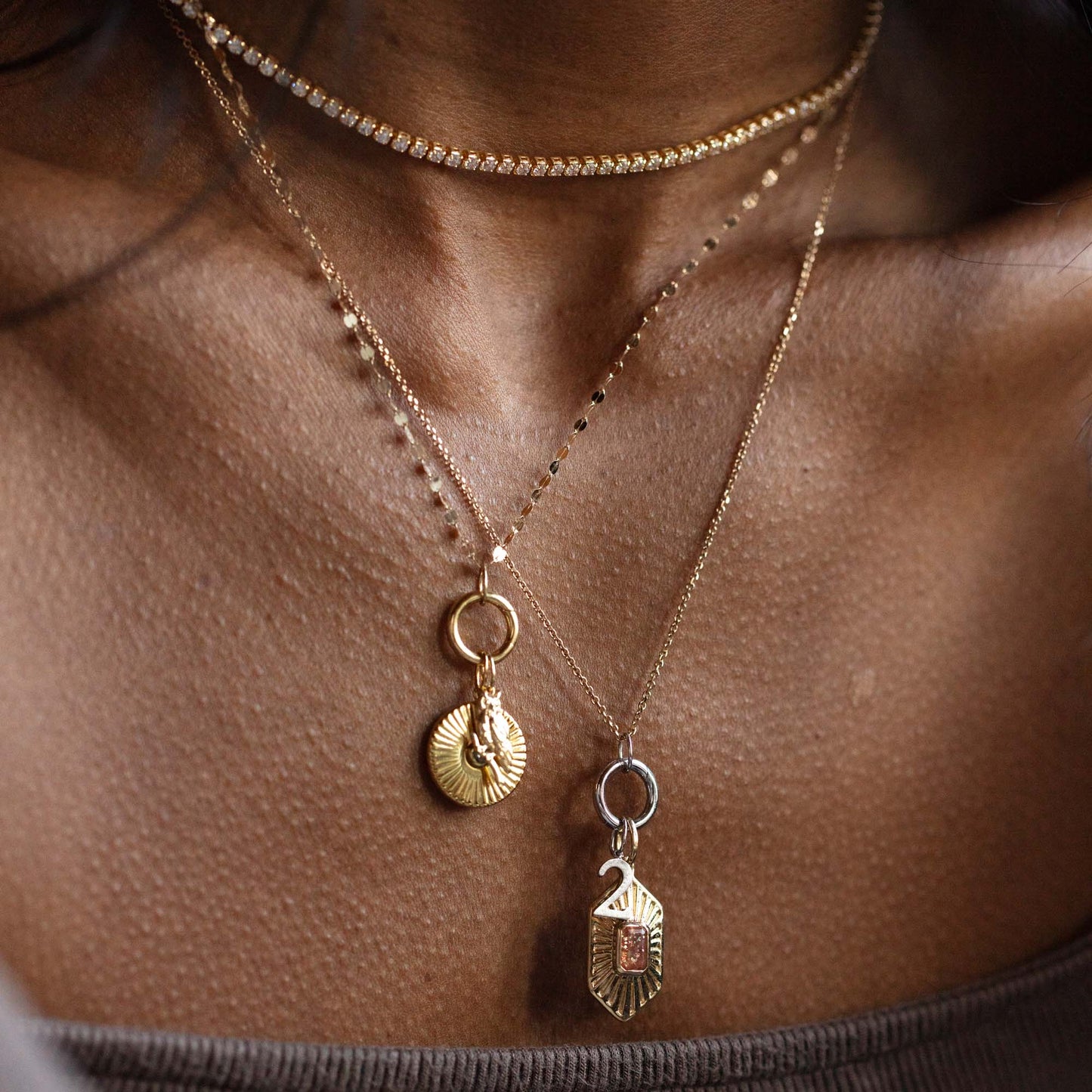 Close-up of a person wearing three layered necklaces, including the Solid Gold Number Charm in White Gold on an engraved rectangular pendant—ideal for those who love personalized jewelry.