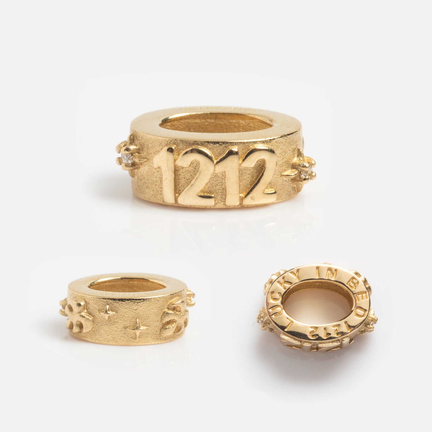 The Solid Gold Angel Number Spacer Charm, a Local Eclectic Exclusive, is shown on a white background with engraved angel numbers (1212), star designs, and the phrase LUCK IN BED.