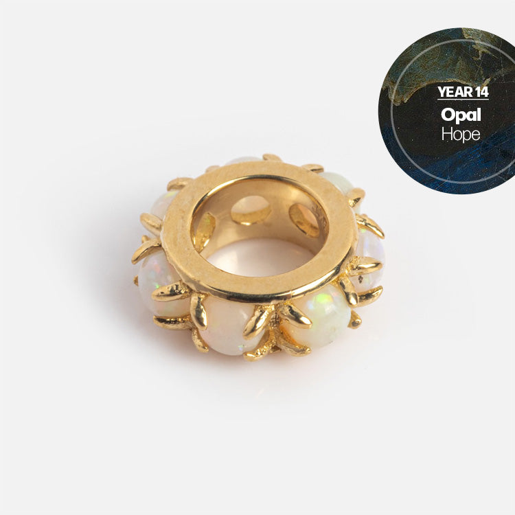 A gold, ring-shaped Solid Gold Anniversaire Charm with opal insets and gold accents is displayed on a white background. A circular label reads Year 14, Opal, Hope, making it a perfect milestone jewelry piece.