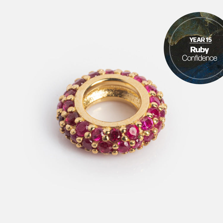 A gold ring adorned with small round rubies and gold beads is displayed on a white background. A label reads: YEAR 15 Ruby Confidence—perfect as milestone jewelry or for your Solid Gold Anniversaire Charm.