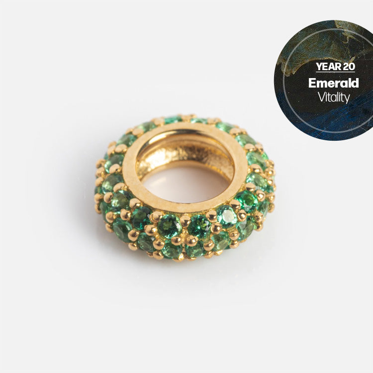 The Solid Gold Anniversaire Charm is a ring-shaped anniversary piece accented with green emeralds and a Year 20 Emerald Vitality label on a marbled background—an ideal milestone jewelry gift for special occasions.