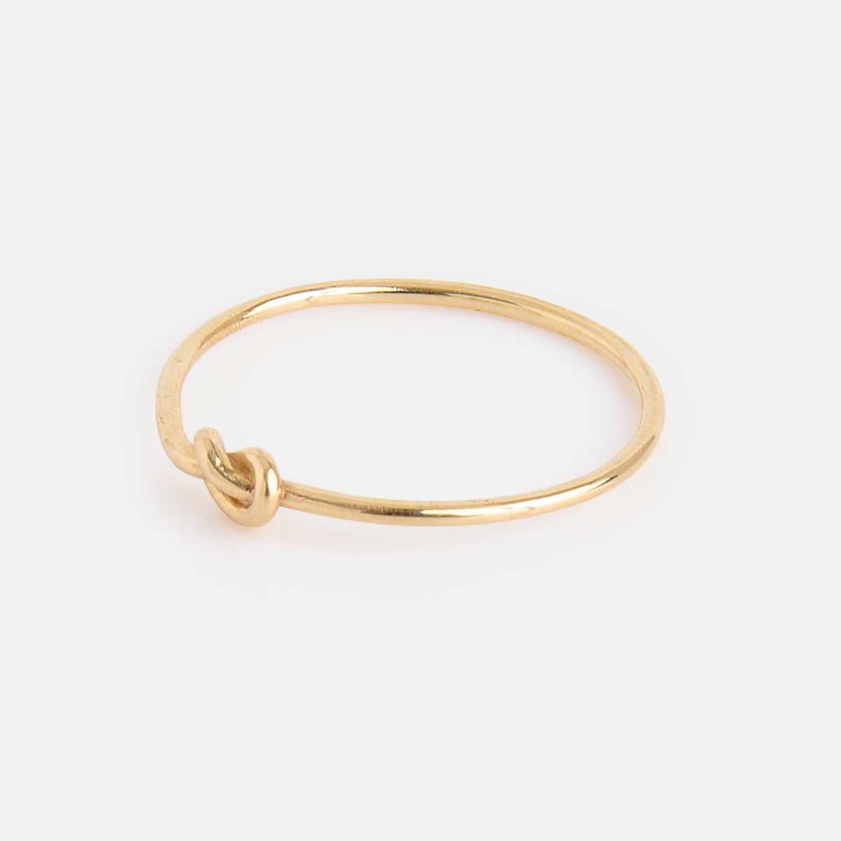The Solid Gold Simple Knot Ring, crafted in thin 10k gold with a small knot detail on one side, is shown against a plain white background.
