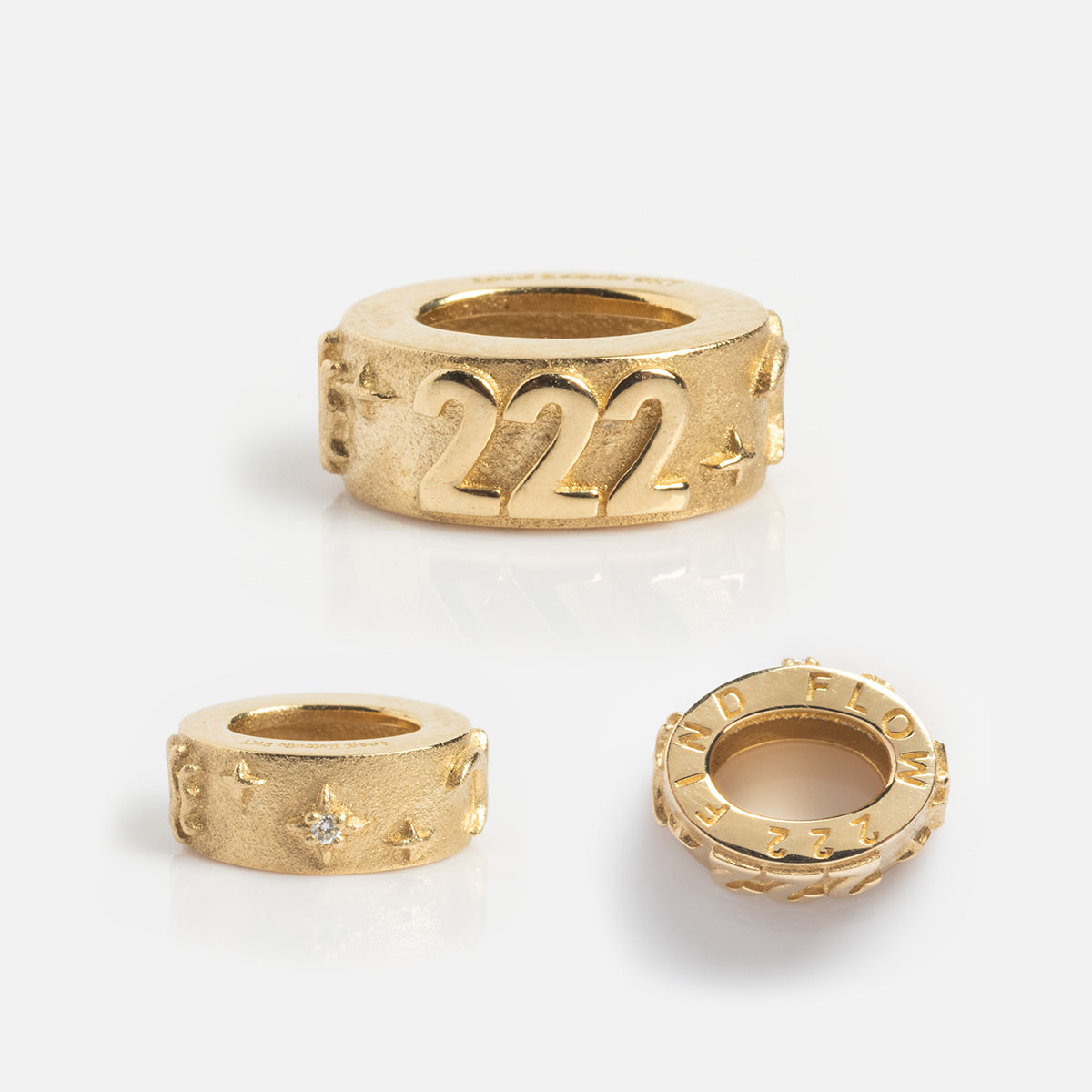 The Solid Gold Angel Number Spacer Charm set features three round gold beads on a white background: the largest displays the 222 angel number, while the others show stars and engraved text around their edges.