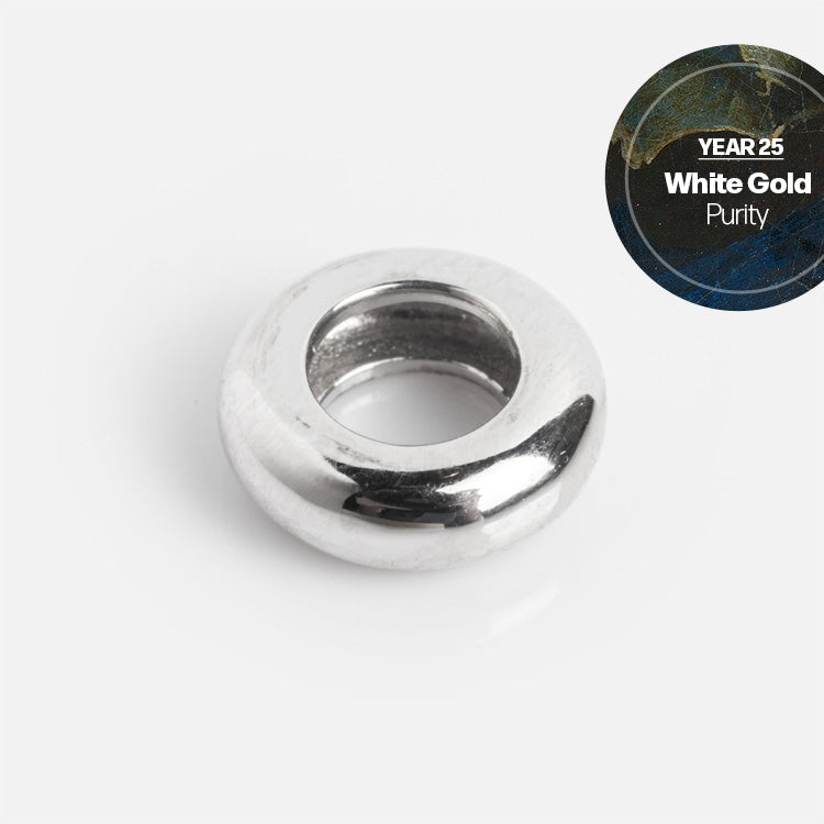 The Solid Gold Anniversaire Charm, a round and smooth white gold bead with a large central hole, is displayed on a white background. A circular label reads: Year 25 White Gold Purity—ideal for milestone or anniversary jewelry.
