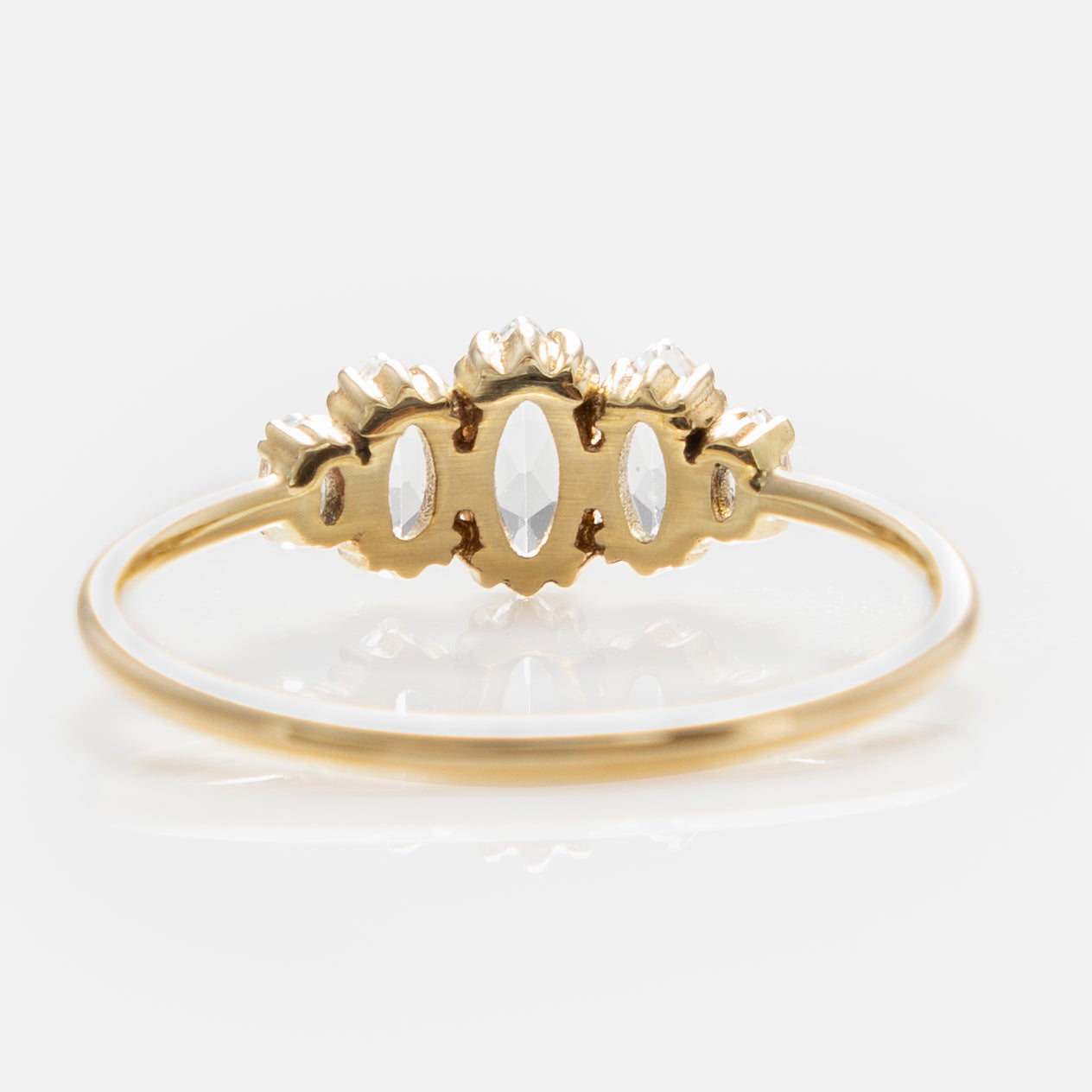 The Solid Gold Essential Marquise Cluster Ring showcases three marquise-shaped clear gemstones in a row with intricate gold accents, photographed on a white background—an elegant, heirloom-quality piece.