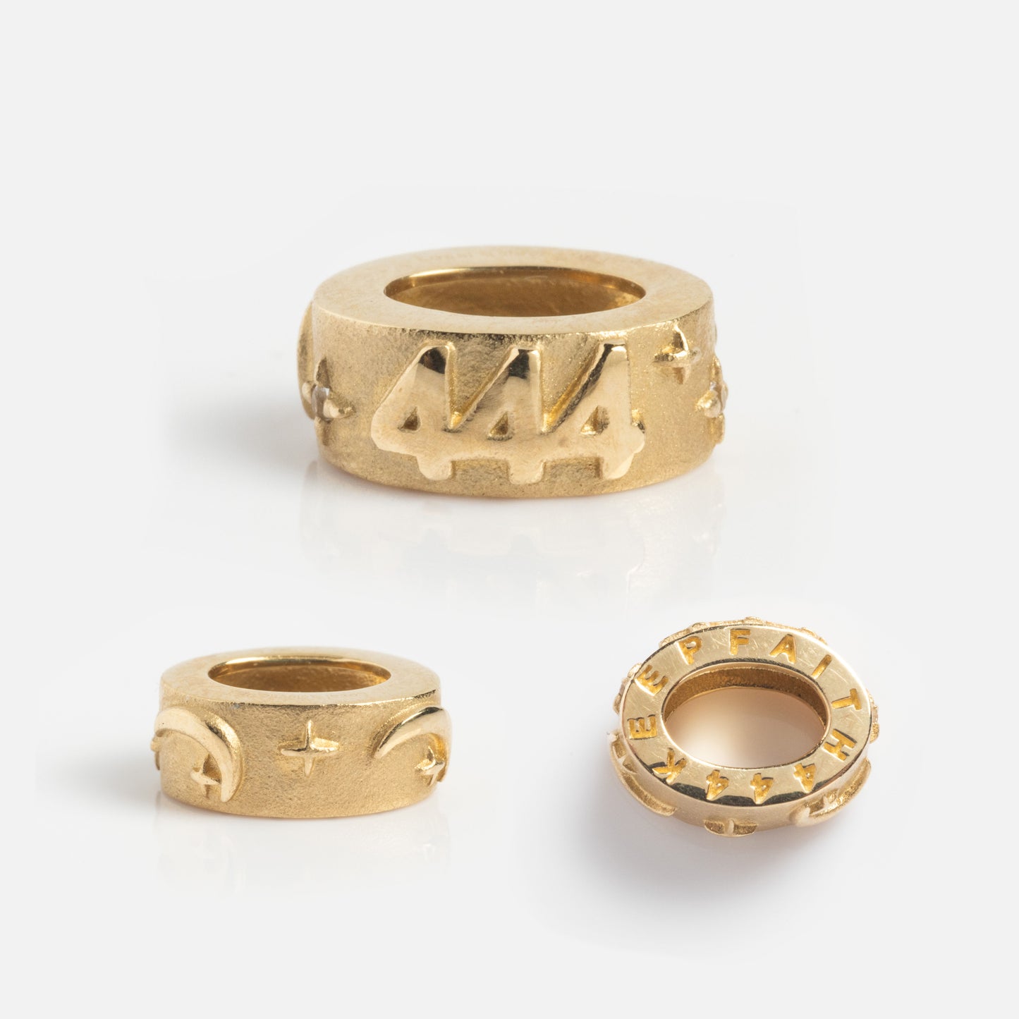 Three gold circular beads are displayed: the largest is a Solid Gold Angel Number Spacer Charm with 444, while the others have plus signs and HEALTH—all Angel Number Charms exclusive to Local Eclectic.