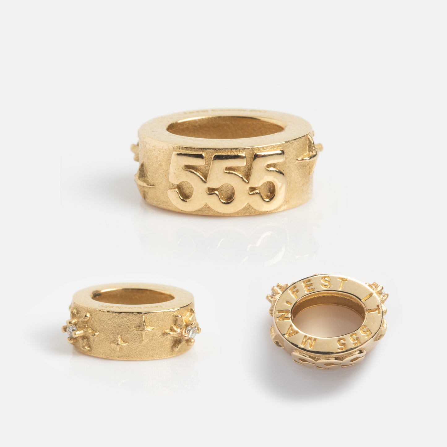 Three Solid Gold Angel Number Spacer Charms are shown on a white background. The front displays 555 and star engravings. A Local Eclectic Exclusive, one charm also features WEST engraved around its edge.