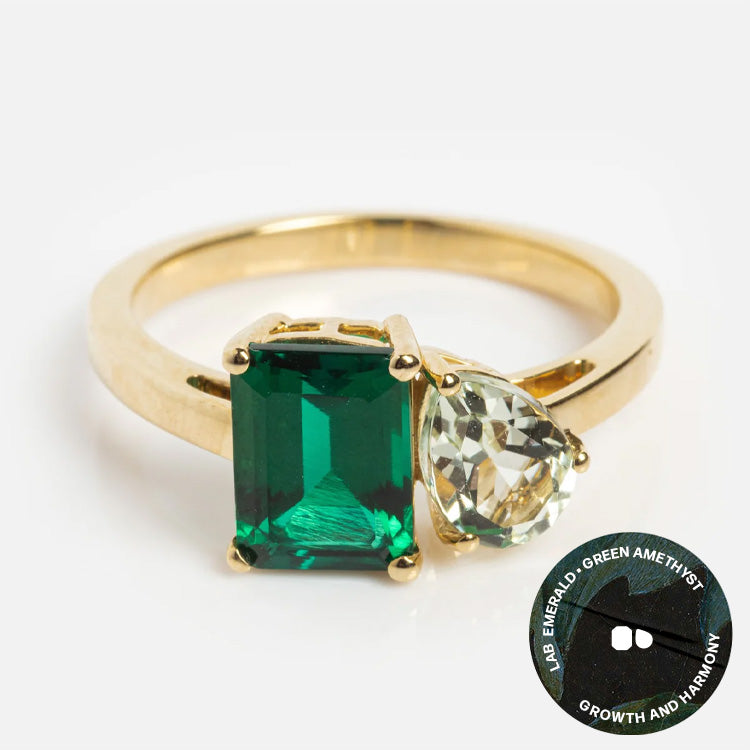 The Solid Gold Toi et Moi Colorful Gemstone Ring features a rectangular lab emerald and a pear-shaped green amethyst, symbolizing growth and harmony with gemstone icons.