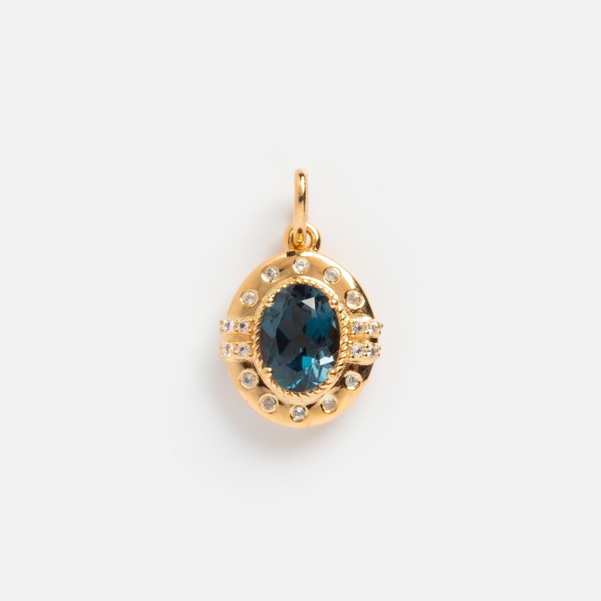 The Vintage Inspired Pendant Charm is a gold oval vermeil piece with a large blue gemstone at the center, surrounded by small white stones, offering classic period appeal in a timeless jewelry design.