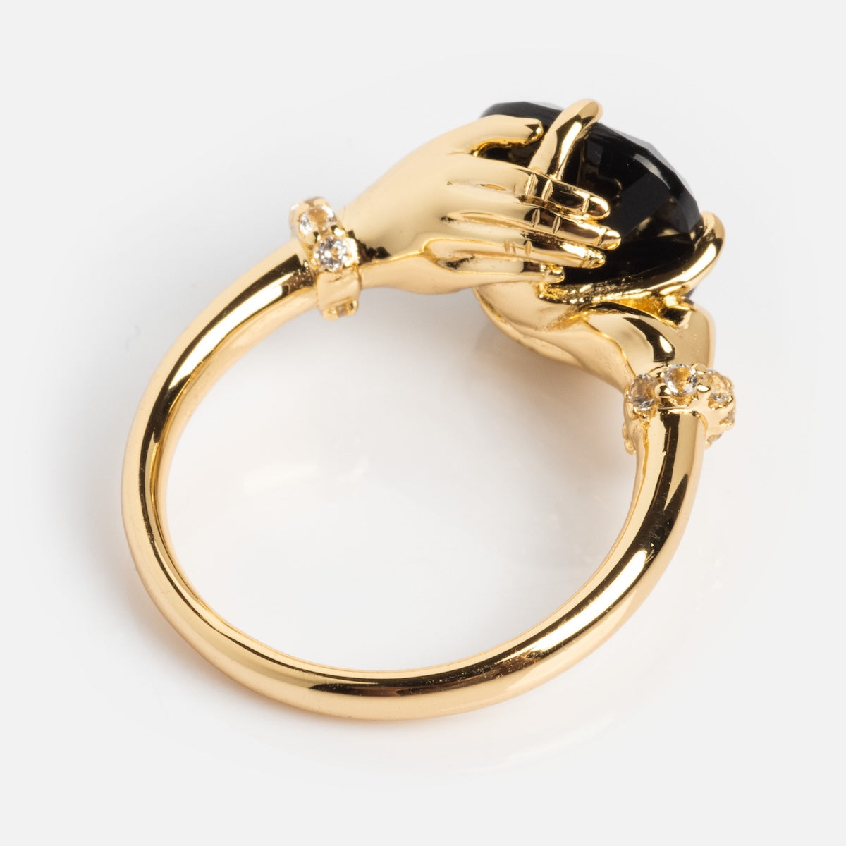 The Past Life Black Spinel Statement Ring features two sculpted hands in gold holding a large black spinel, accented with small clear stones at the wrists for a vintage-inspired look.