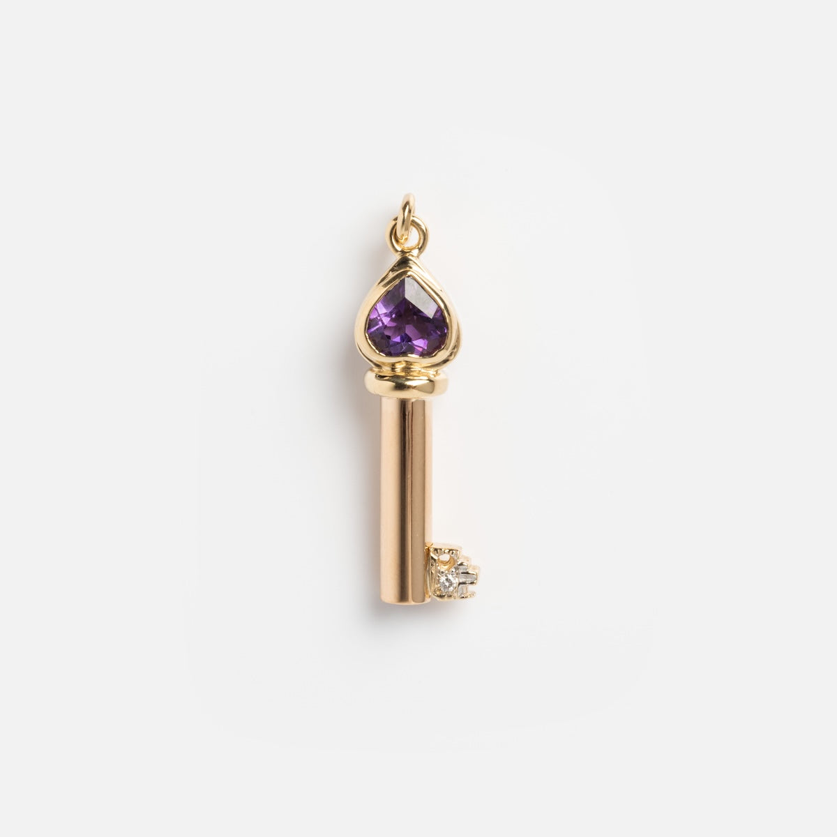This vintage 18k yellow gold heart key charm features an amethyst gemstone and a clear stone accent, complete with a loop for attaching to your favorite chain.