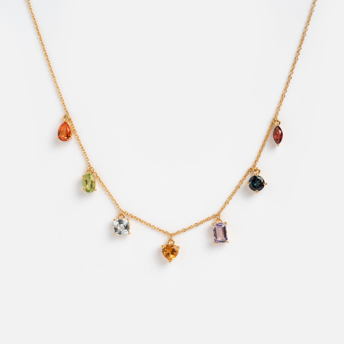 The Classical Confetti Gemstone Necklace is a vintage-inspired 14k gold vermeil piece featuring seven distinct gemstone charms, each uniquely shaped and colored, evenly spaced along the chain against a white background.