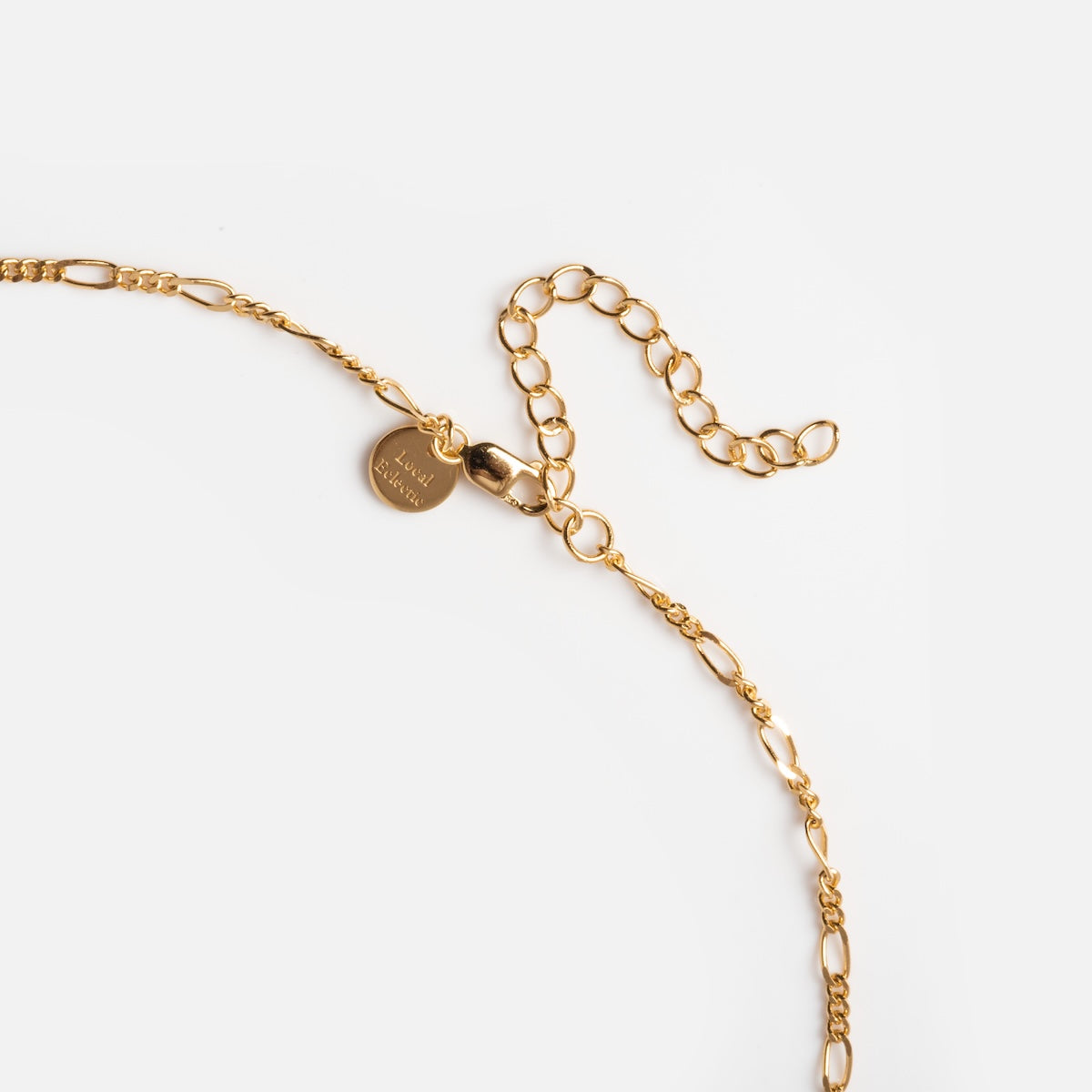 A close-up of the Sonnet Safety Pin Charm Holder Necklace, showcasing its gold chain with an adjustable clasp and a small round charm, exuding art deco elegance against a white background.