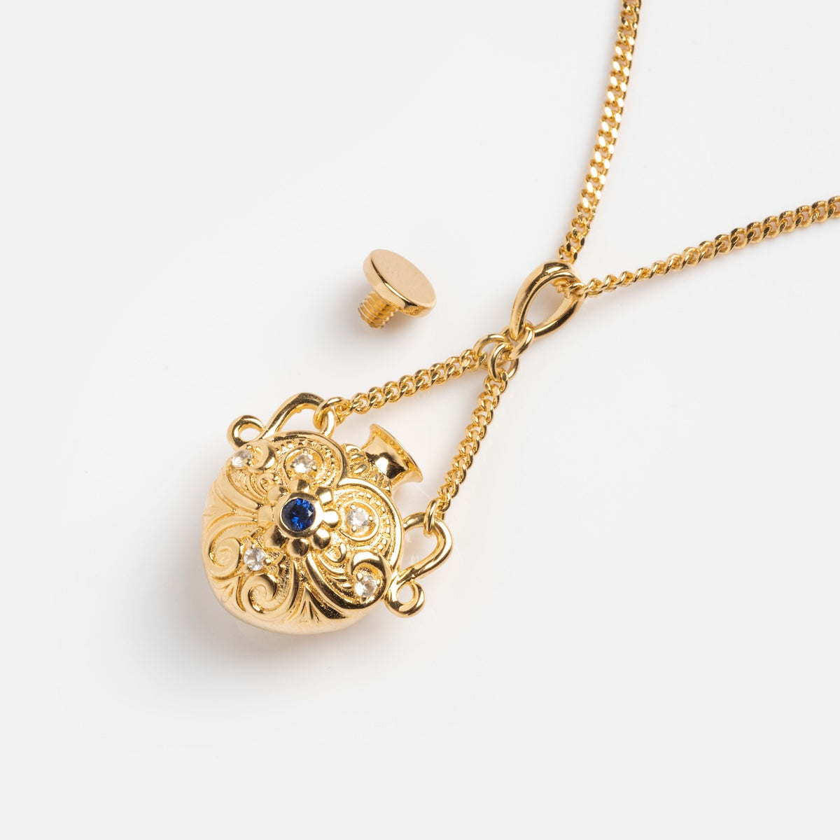 The Juliet Vial Pendant Necklace features a vintage-inspired gold floral pendant with a blue sapphire centerpiece, shown with its removable screw top beside it and hanging from a gold chain on a white background.