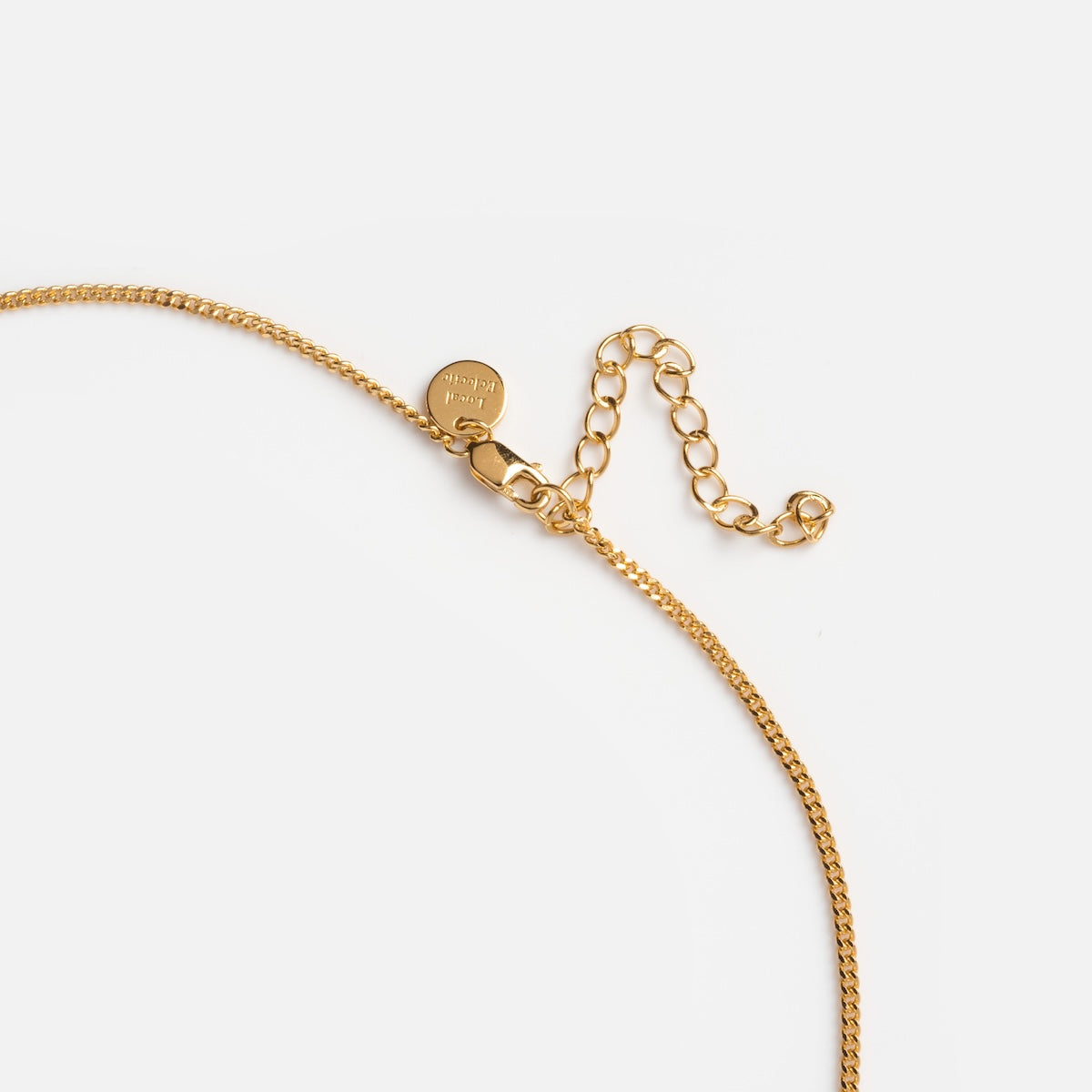 A close-up of the Rose’s Blue Sapphire Heart Locket, a gold chain necklace with an adjustable clasp and engraved round tag, displayed on a white background next to a pearl-accented necklace for added elegance.