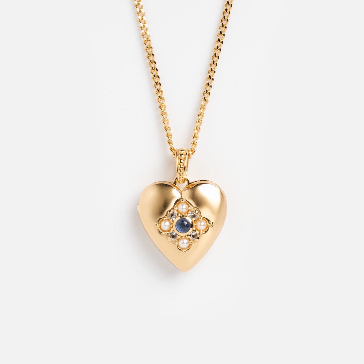 Rose’s Blue Sapphire Heart Locket is a gold vermeil heart locket necklace with a cluster of blue sapphires in a floral pattern at the center, shown on a simple gold chain against a plain white background.