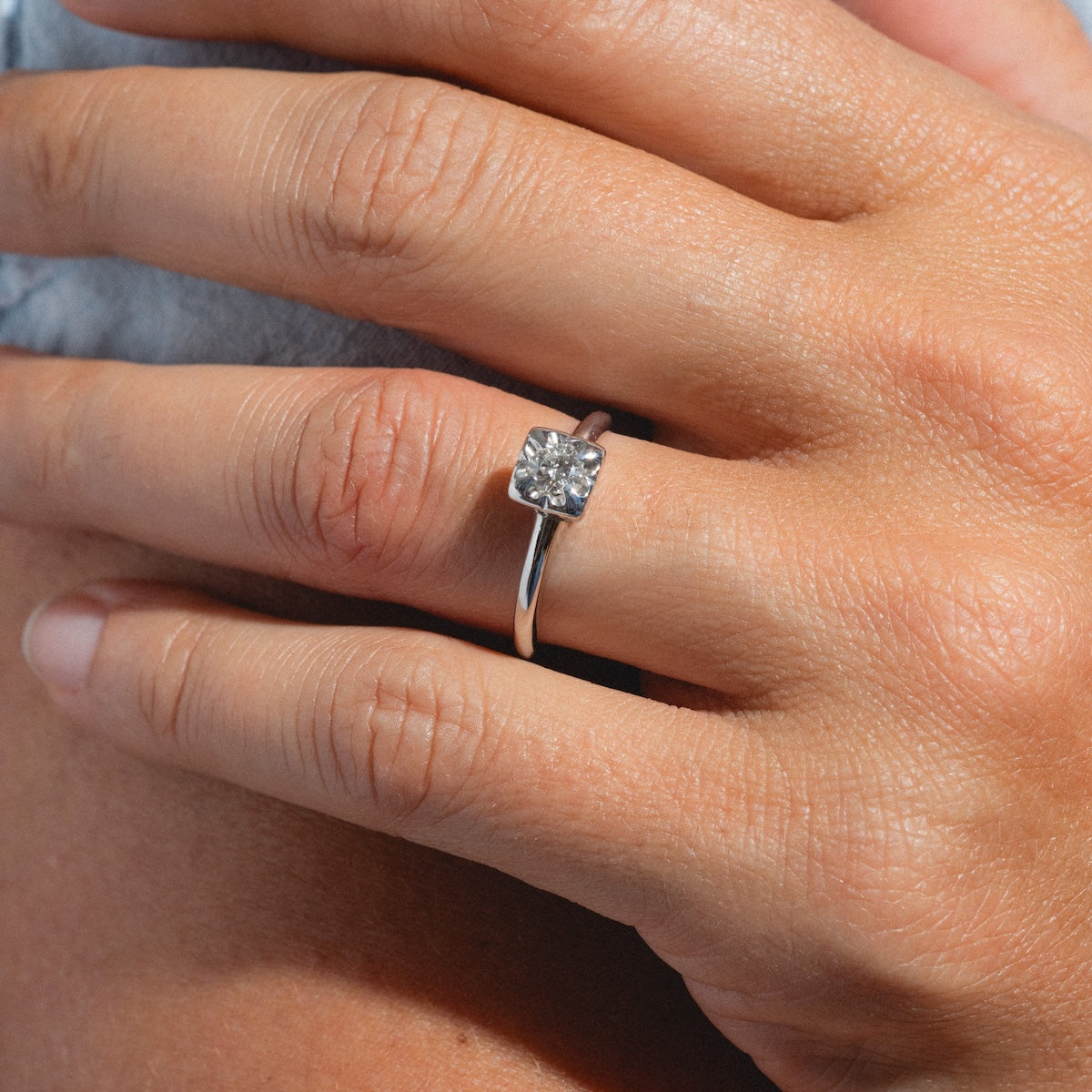 A close-up of a hand wearing the Vintage 14k 1940s White Gold Square Set Diamond Ring, size 7, featuring a single diamond on the ring finger against a blurred background.