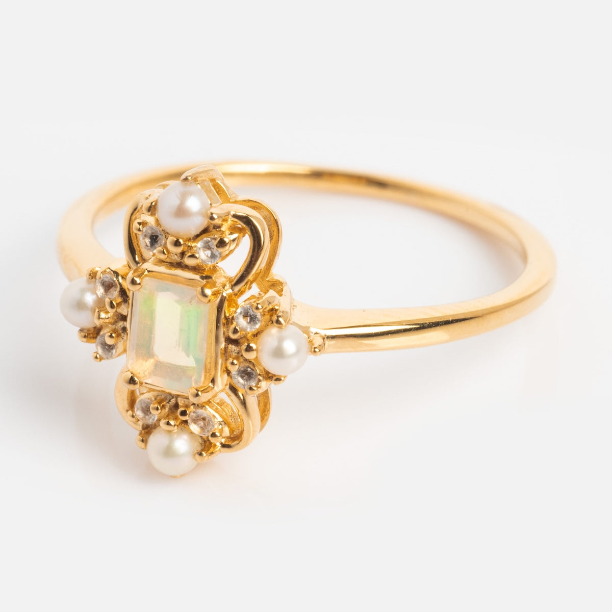 The Crown Jewel Opal and Pearl Ring showcases a rectangular opal center, encircled by white pearls and clear gems, all set in 14k gold vermeil for a vintage, period-inspired look.