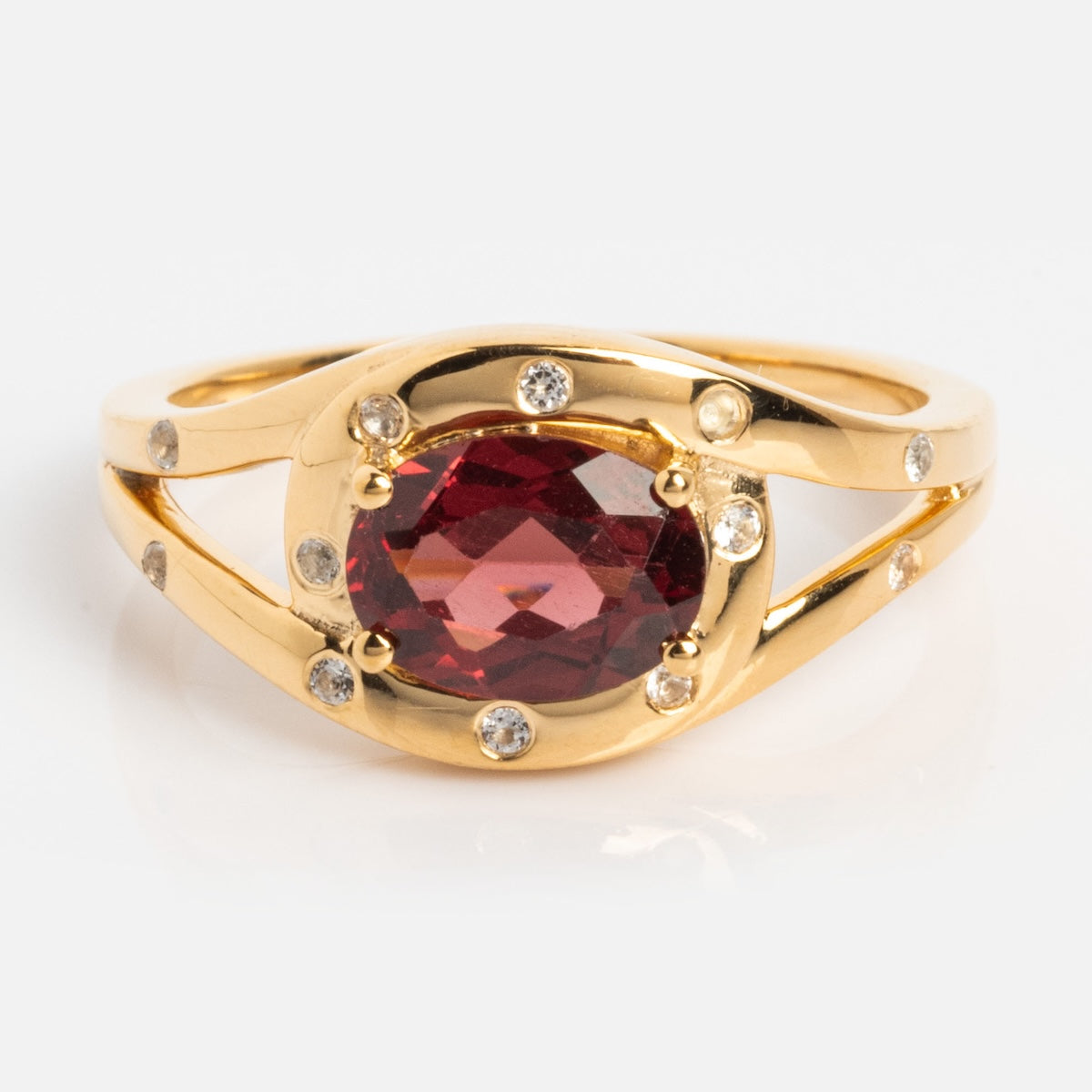 The Golden Age Garnet Cocktail Ring is a vintage-inspired gold vermeil piece with a large oval garnet centerpiece, small round white stones, and a split shank band.