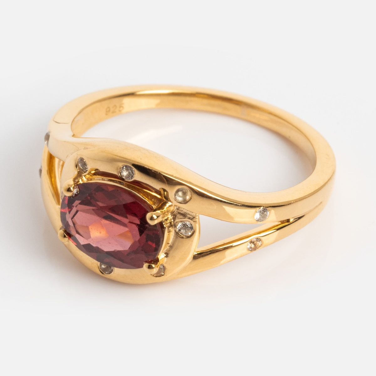The Golden Age Garnet Cocktail Ring is gold vermeil with a large oval red gemstone at the center, accented by small clear stones on the band, and shown on a plain white background.
