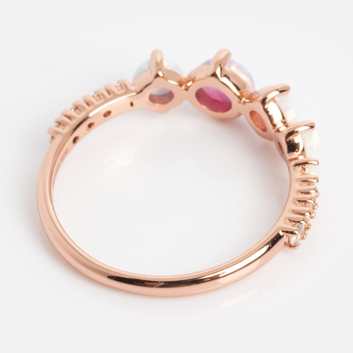 The Pastel Opal Shooting Star Ring in rose gold vermeil is shown from the side, highlighting prong-set oval and round gemstones on a smooth, polished band with intricate setting details.