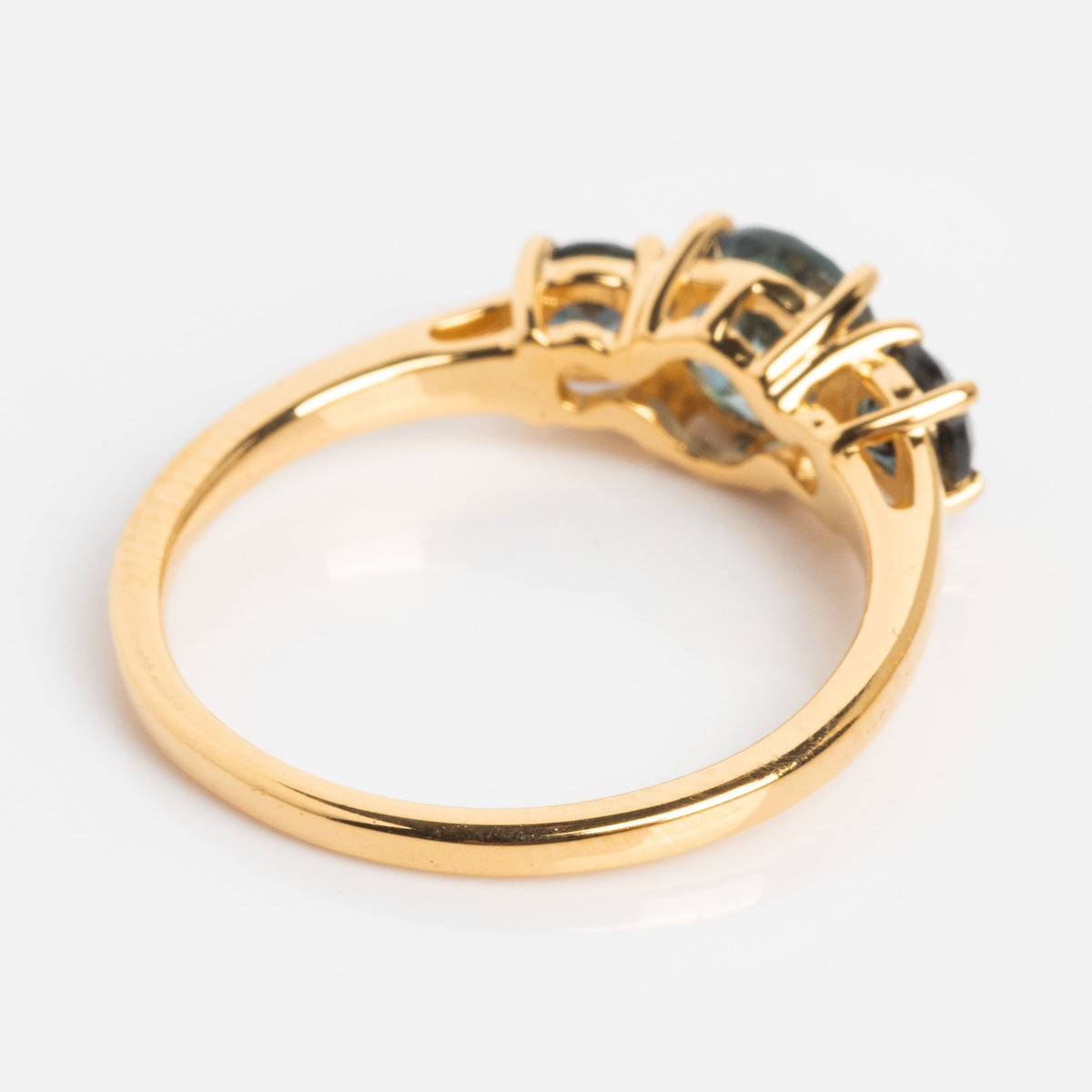 The London Blue Topaz Trilogy Ring features a smooth gold band with three round London blue topaz gemstones set in prongs, displayed on a white background.