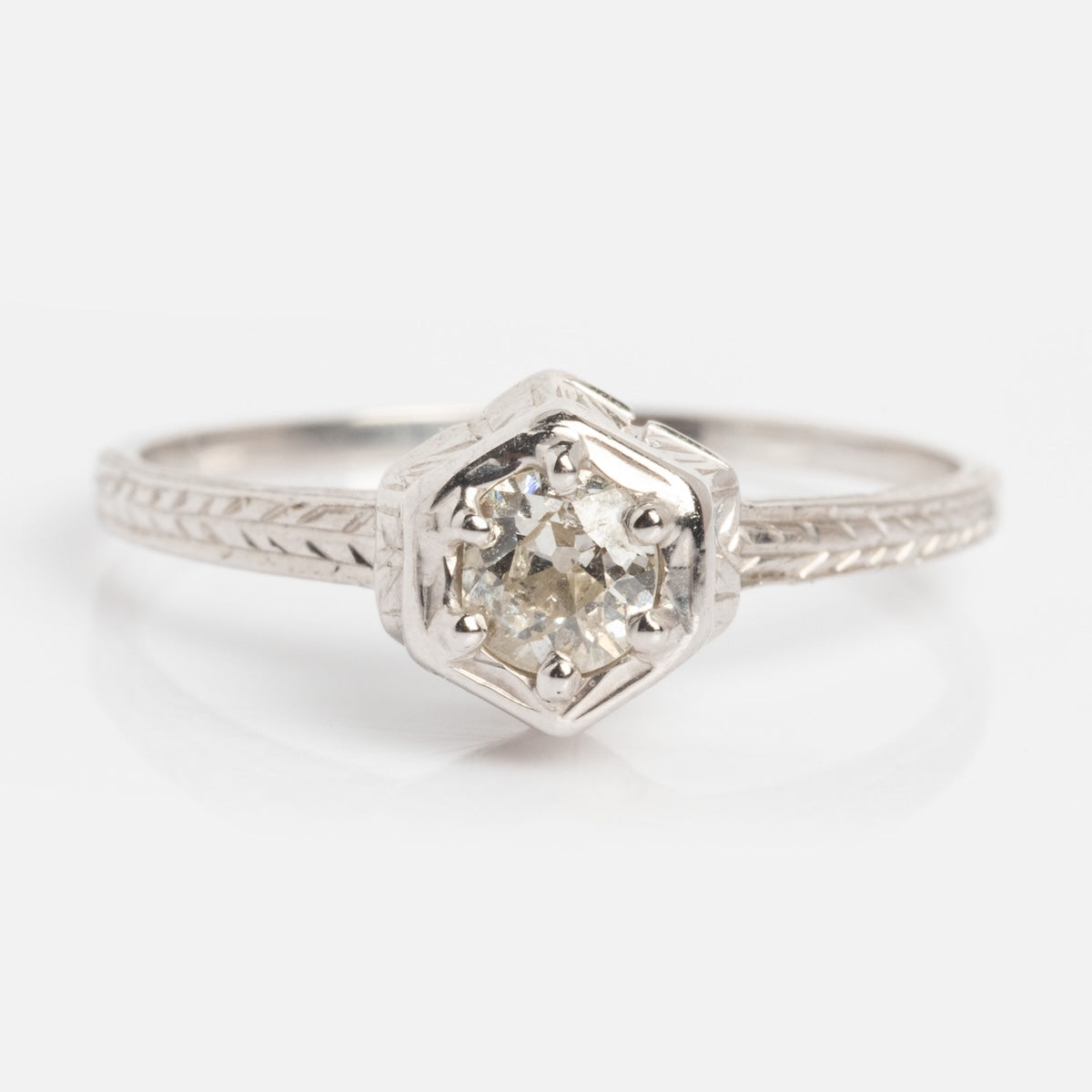 The Vintage 18k White Gold Hexagon Set Diamond Ring, size 7, features a round diamond in a hexagonal setting and detailed engraving on the band.
