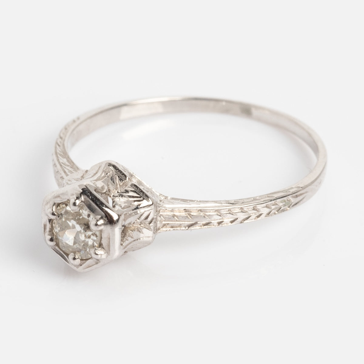 The Vintage 18k White Gold Hexagon Set Diamond Ring, size 7, features a round-cut diamond in a hexagonal setting on an intricately engraved white gold band. Shown against a plain white background.