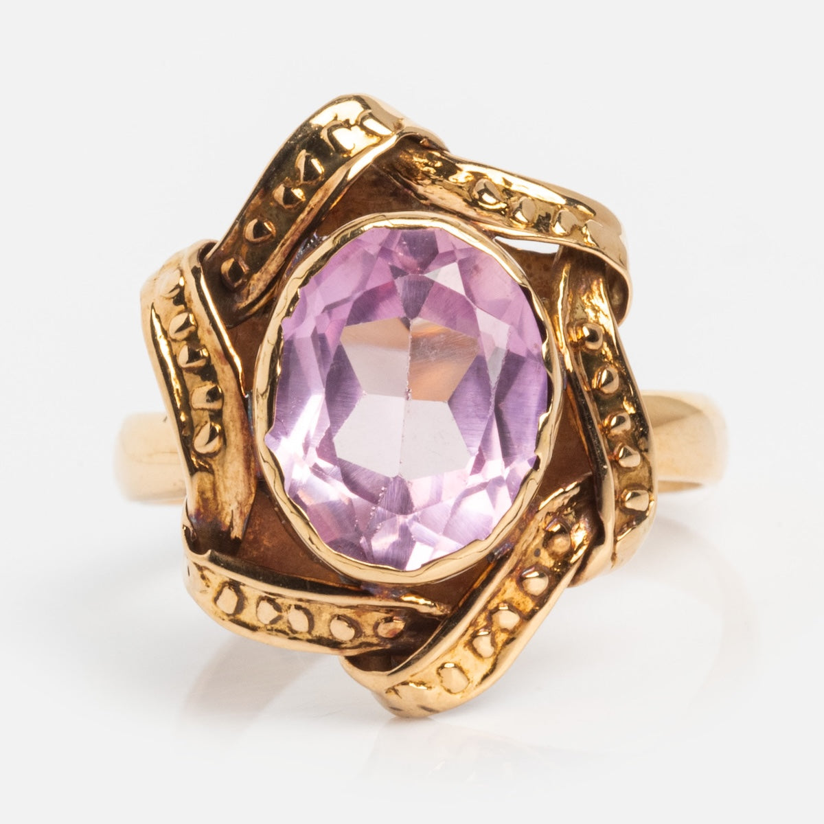 A vintage 18k gold ring from the 1890s features an ornate textured band and a large faceted oval pink sapphire at its center, capturing the opulence of Gilded Age jewelry. Size 6.5.