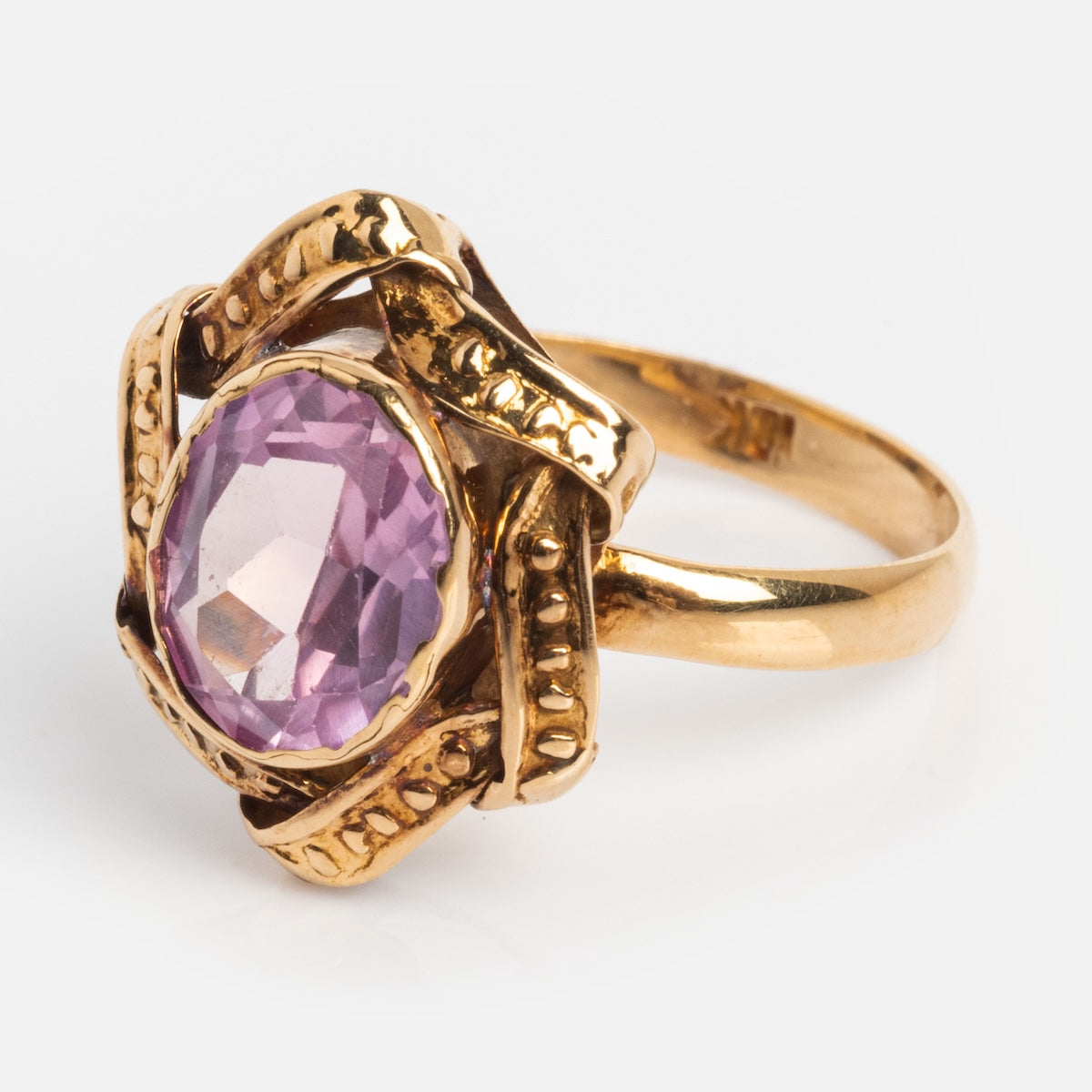 A Vintage 18k 1890s Opulent Pink Sapphire Cocktail Ring (Size 6.5) showcases a large oval-cut pink sapphire in an ornate, textured gold band with decorative twists—evoking the elegance of Gilded Age jewelry.