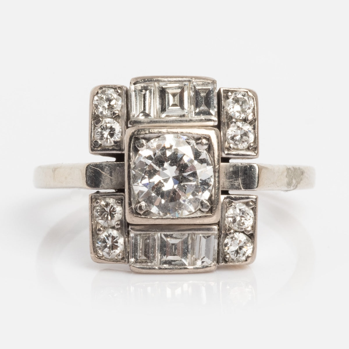 The Vintage 18k 1930s Art Deco Geometric Diamond Ring Size 9 features a bold geometric design with a large central diamond, accented by smaller round and rectangular diamonds in elegant 18k white gold.
