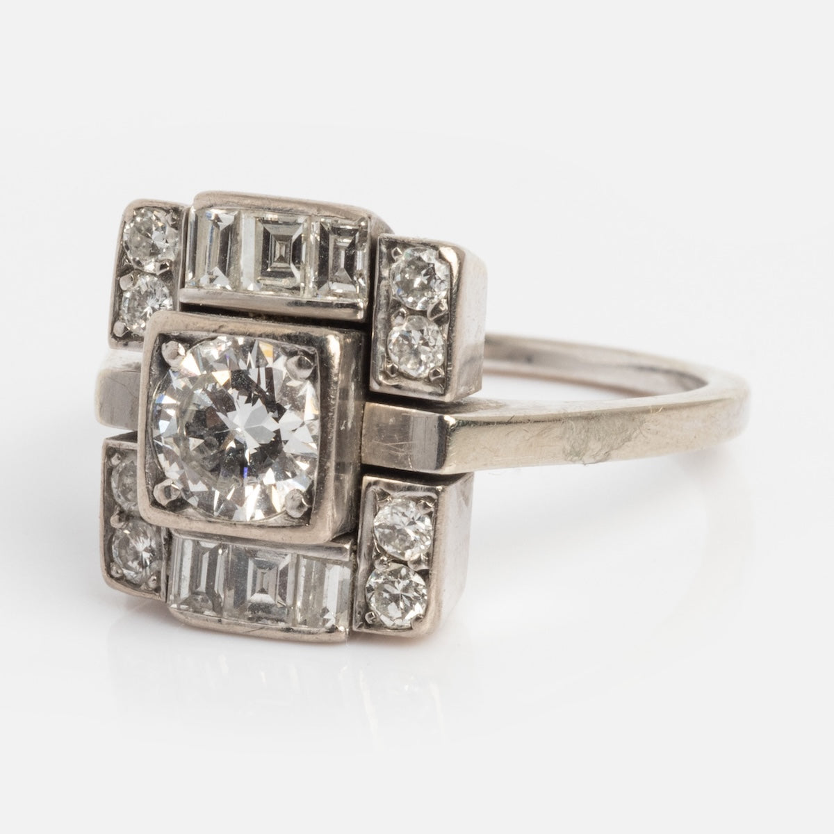 The Vintage 18k 1930s Art Deco Geometric Diamond Ring, size 9, showcases a bold geometric design with a prominent central diamond surrounded by smaller round and rectangular diamonds in white gold.