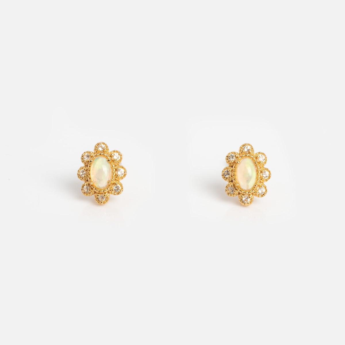 The Opal Majesty Studs are vintage-inspired gold earrings with oval Ethiopian opals at the center, encircled by a floral halo of small round gems. Shown on a plain white background.