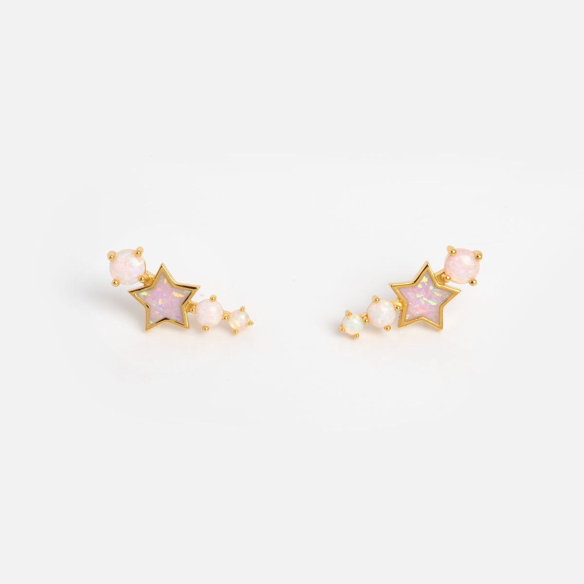 The Pastel Opal Shooting Star Studs feature a central star shape with pink stones, accented by smaller round pink opal studs arranged in a curve beside each star, shown against a plain white background.
