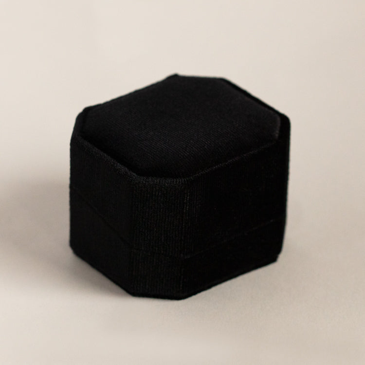 The Fancy Velvet Ring Box, featuring a black hexagonal design in velvet, sits closed on a light neutral surface.