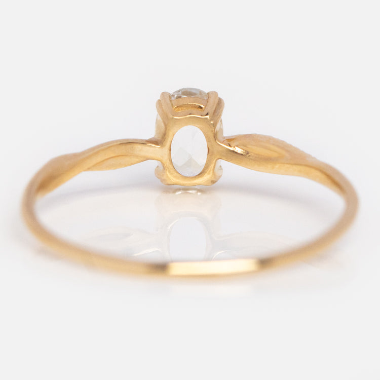 The 14k Delicate Twist Ring features a slim, twisted 14k gold band with an oval clear gemstone at the center, displayed against a white background.