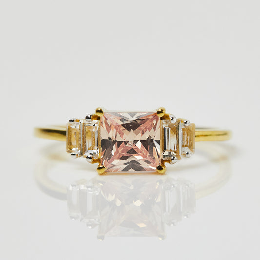 The Morganite and White Topaz Deco Ring features a square-cut pink morganite center stone and rectangular white topaz accents, set in yellow gold vermeil and displayed on a luminous, reflective surface.