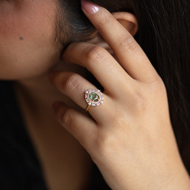 A close-up of a womans hand touching her face, highlighting the Fern Green Topaz Statement Ring with Pearl Halo. This luxury jewelry piece features a vivid green topaz surrounded by elegant pearls on 14k gold vermeil.