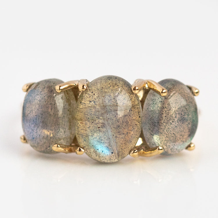 The Sweetest Gumdrop Ring features three large oval natural labradorite gemstones with a blue-gray iridescent sheen, set side by side in yellow gold and each secured by four prongs, displayed against a white background.