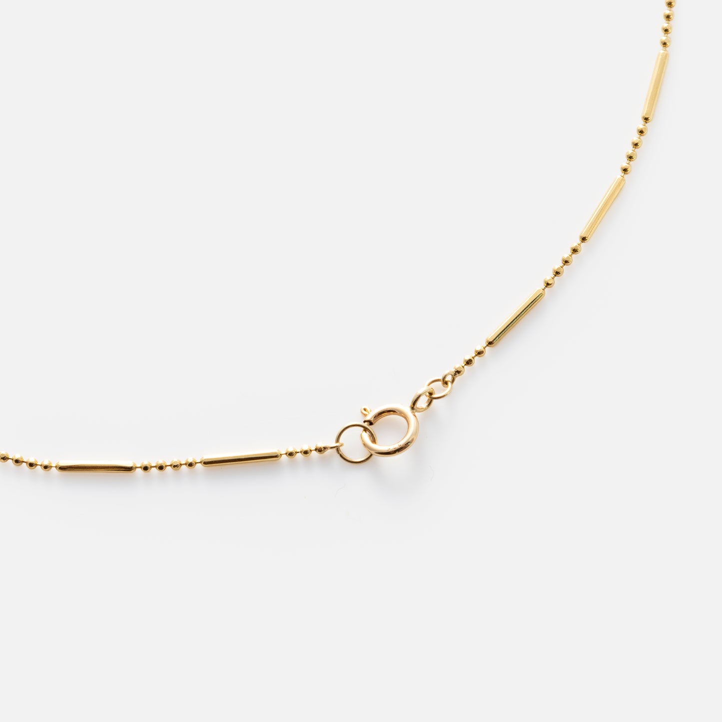The Solid Gold Dot Dash Chain is a delicate 9k gold necklace with small round and tube-shaped links, secured by a spring ring clasp and shown on a white background.