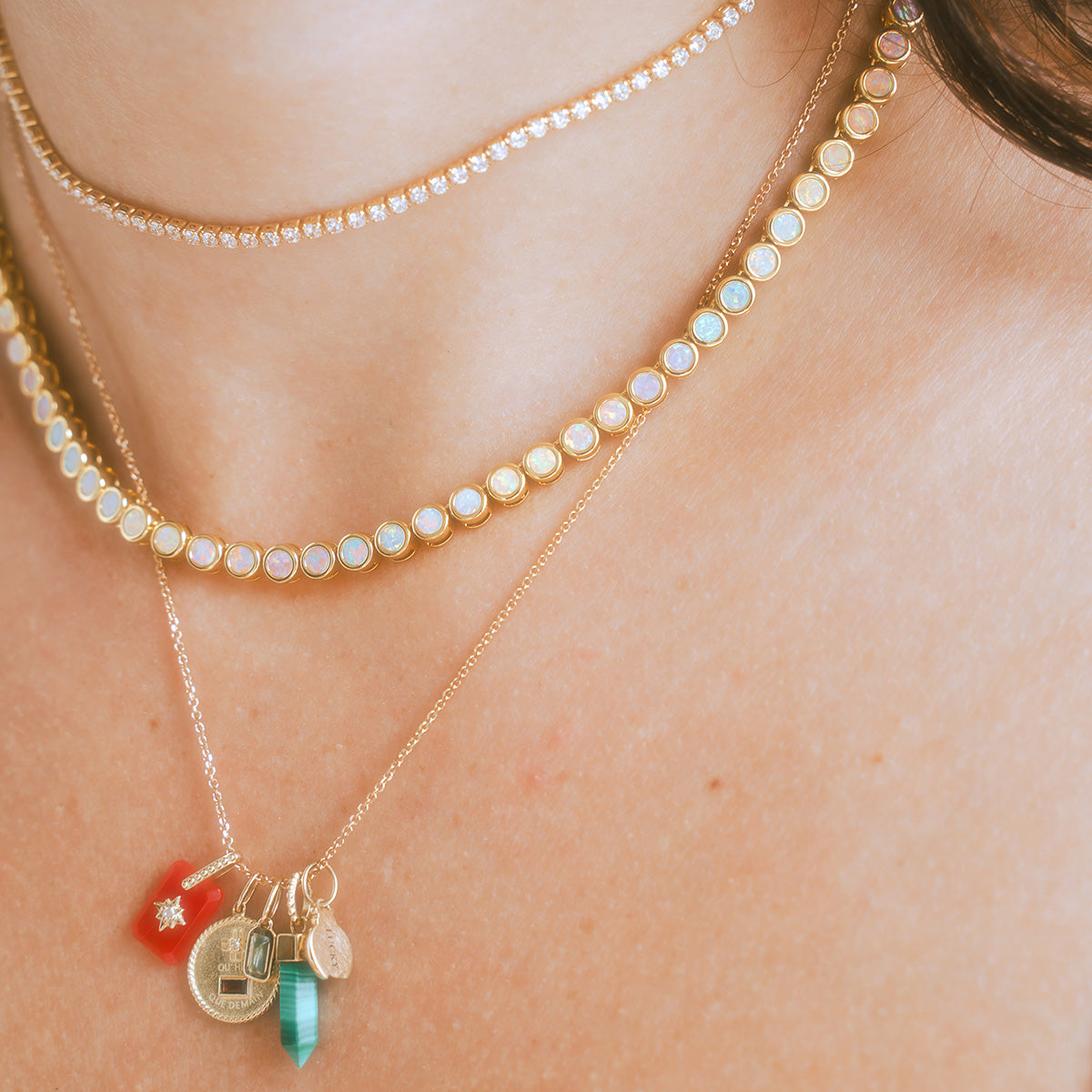 A close-up of a neck layered with four gold necklaces: two with round gemstones, one with a row of diamonds, and one featuring unique pendants like turquoise, a red charm, and a Solid Gold Birthstone Baguette Charm for personalized style.