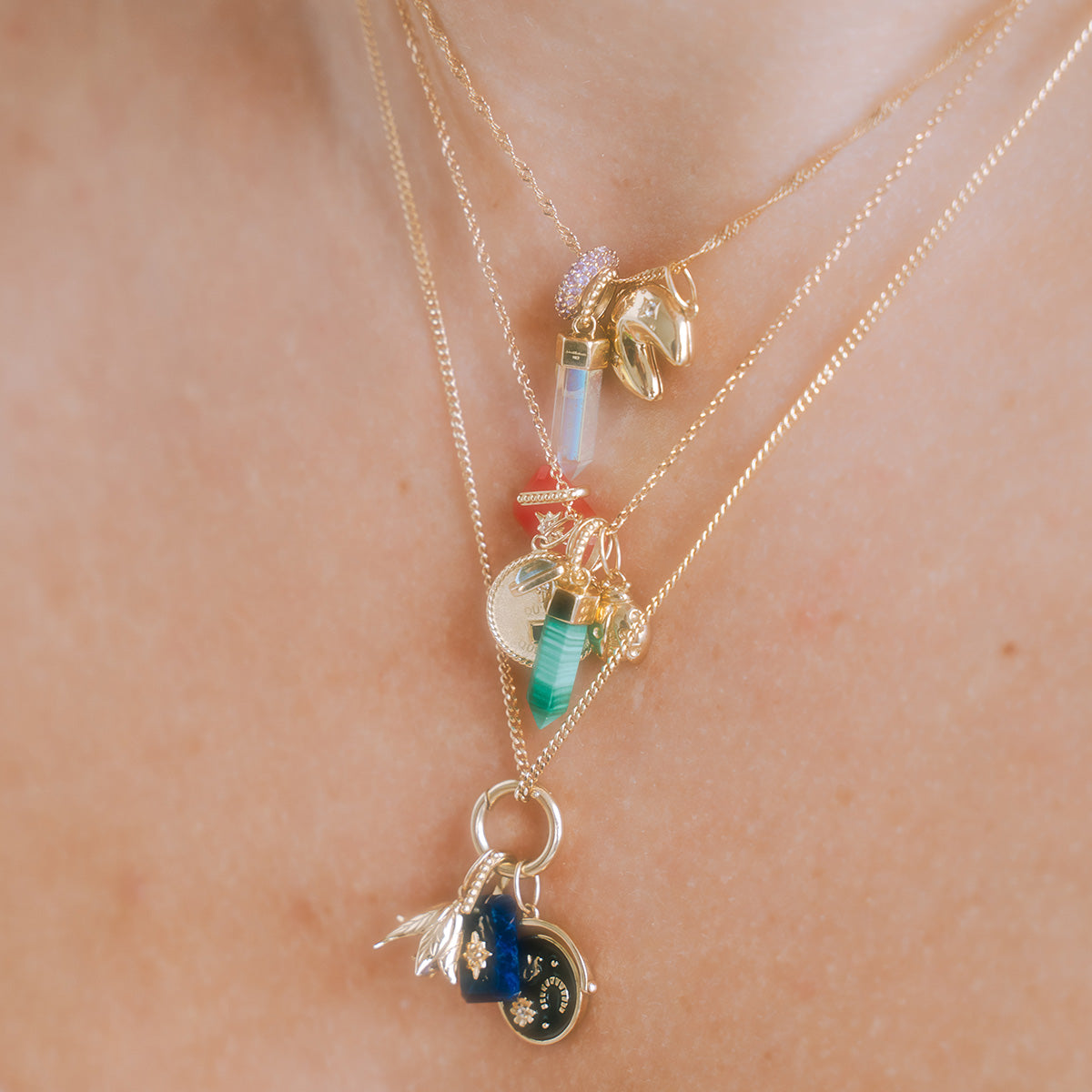 A close-up of a neck adorned with layered gold necklaces, including the Solid Gold Crystal Amulet Charm for Manifestation and other colorful pendants. The softly lit skin highlights each unique charm clearly.